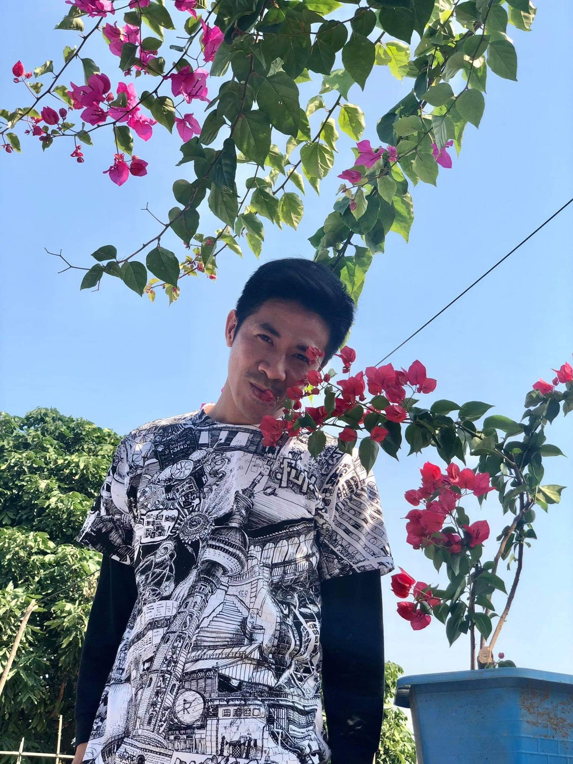 vietnamese young man wearing black and white all over printed BERLIN city t-shirt by heiner radau, smelling red pink flowers