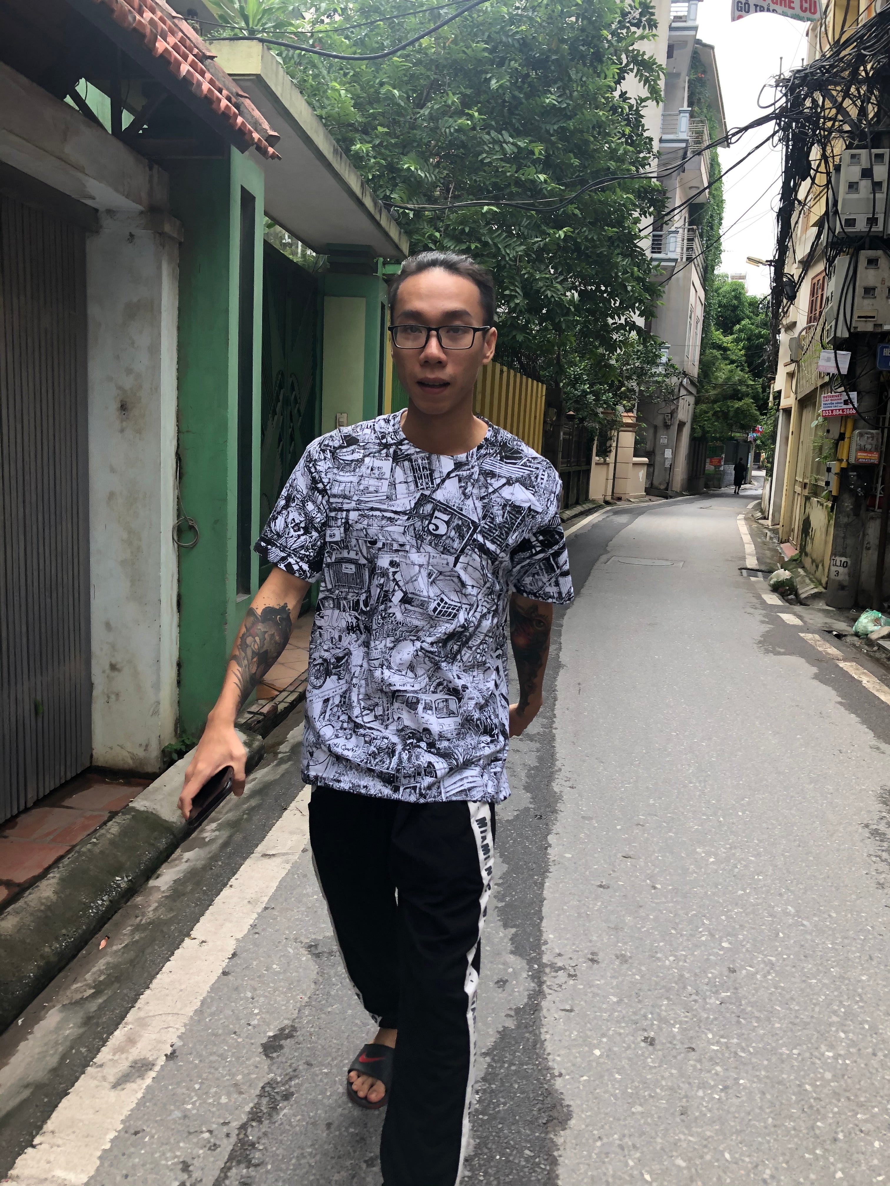 vietnamese young man wearing black and white all over printed HANOI city t-shirt by heiner radau walking through the alleys of tay ho